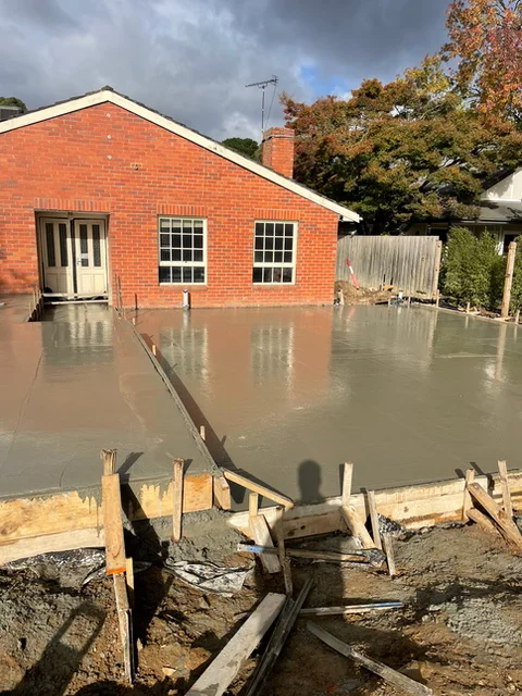 Freshly poured concrete slab for a ground floor extension against an existing brick home