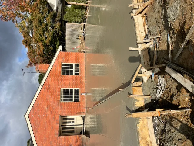 Freshly poured concrete slab for a ground floor extension abutting the rear wall of an existing brick home